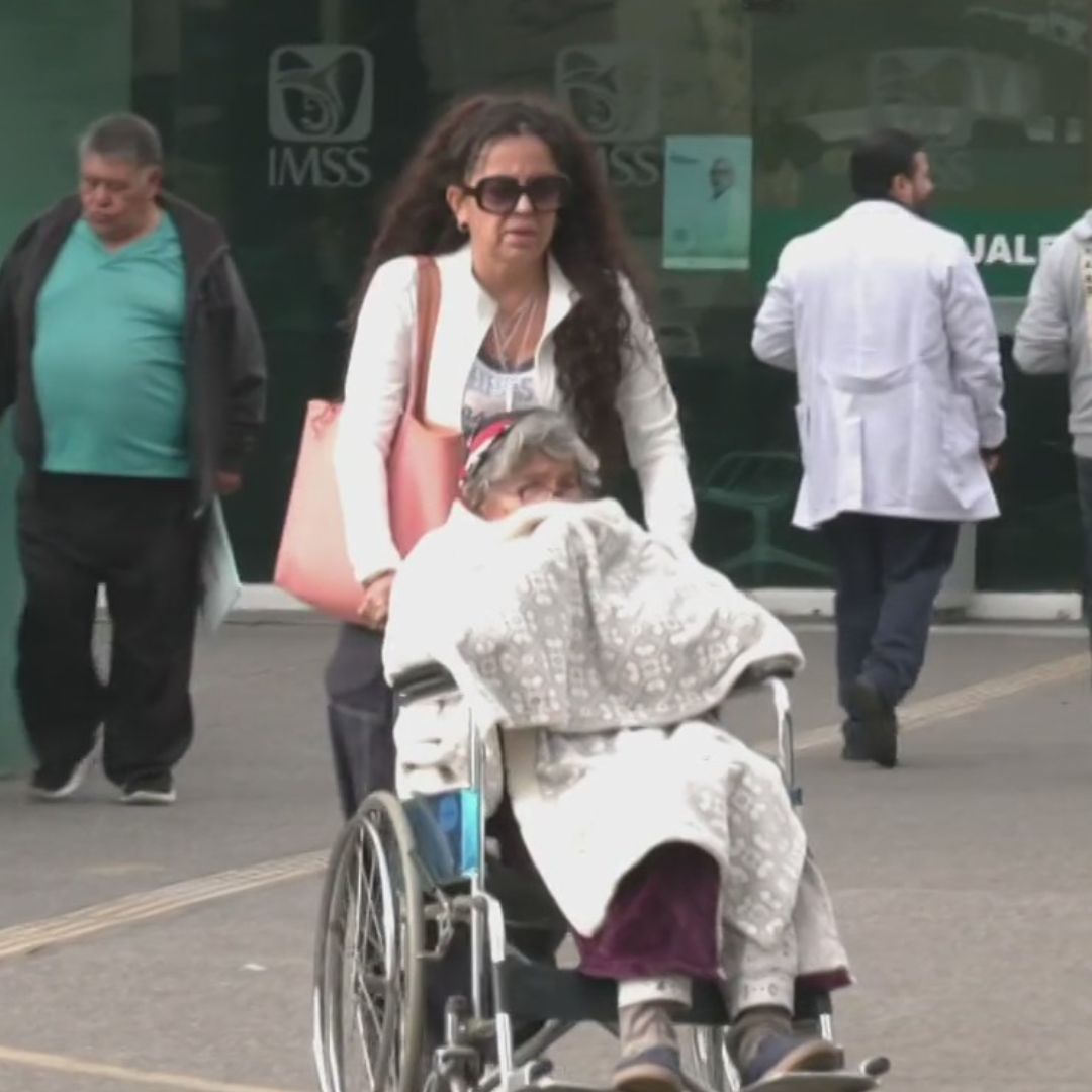 La señora Ebelia sale de una clínica en silla de ruedas.